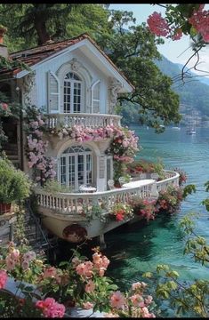 a house on the water with flowers growing out of it's windows and balconies