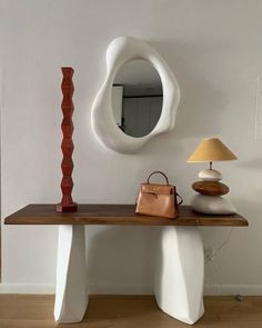 a table with a mirror, lamp and handbag on it in front of a white wall