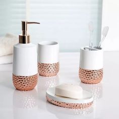 a bathroom set with white and rose gold bath accessories on a counter next to a towel dispenser, soap dispenser and toothbrush holder