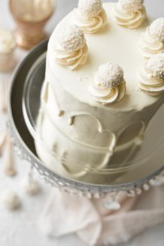 a white cake with frosting on top is sitting on a silver platter next to utensils