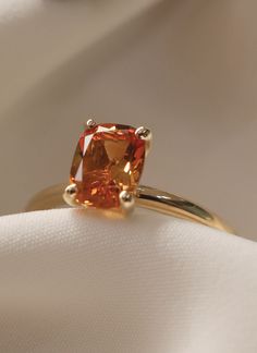 an orange diamond ring sitting on top of a white cloth