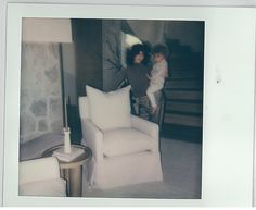 two people standing in a living room next to a white chair