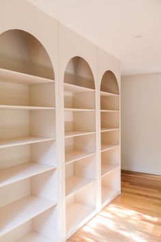 an empty room with white bookcases and hard wood floors