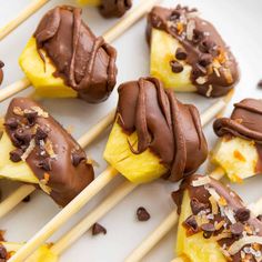 chocolate covered pineapples on wooden sticks with toppings