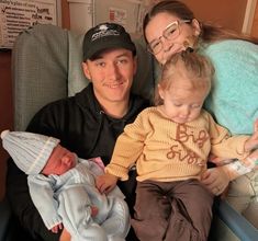 a man and woman sitting next to a baby in a hospital bed holding two babies