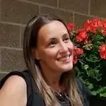 a woman sitting next to a potted plant with red flowers in it and smiling at the camera