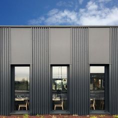 the side of a building with three windows and tables in front of it, against a blue sky