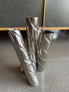 two silver vases sitting on top of a gray floor in front of a wall