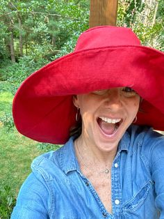 a woman wearing a large red hat on top of her head in front of trees