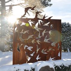 a wooden sign with birds flying over it in the snow and sun shining through trees