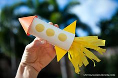 a hand holding up a paper rocket with yellow dots on the outer part and an orange top