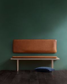 a brown leather bench sitting on top of a wooden floor next to a green wall