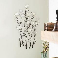 a metal wall sculpture with white flowers on it's side next to a fireplace