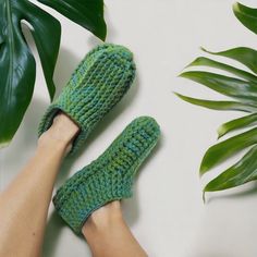 a person wearing green knitted slippers next to a plant