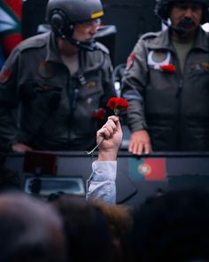 a person holding a red rose in front of two uniformed men with helmets on their heads