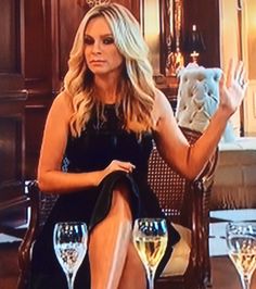 a woman sitting in a chair with two wine glasses on her feet and one hand up