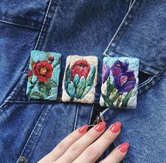 a woman's hand with red nails and blue jeans holding onto some colorful flowers