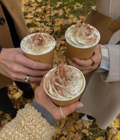 three people holding drinks in their hands with autumn leaves on the ground behind them,