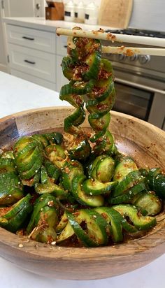 a wooden bowl filled with green vegetables on top of a white counter next to an oven