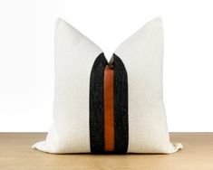 a black and white pillow with an orange stripe on the side sitting on a wooden table