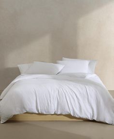 a bed with white linens and pillows in a neutral colored room, against a beige wall