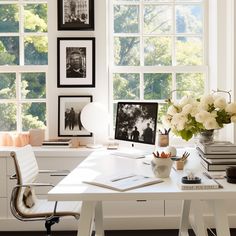 a white desk with flowers and pictures on the wall next to it in front of a window