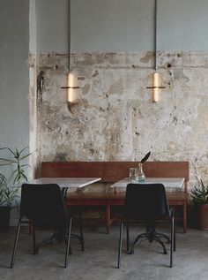 two tables and chairs are in front of a brick wall with potted plants on it