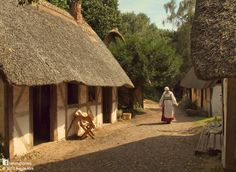 a woman walking down a dirt road next to small houses with thatched roof tops