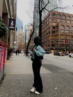 a woman is standing on the sidewalk looking at her cell phone and buildings in the background