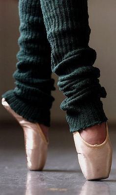 the legs and ankles of a woman in ballet shoes, with their feet covered by leg warmers