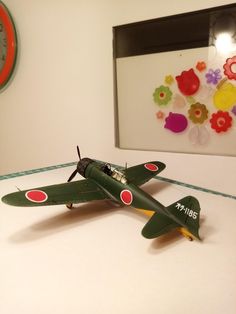 a model airplane sitting on top of a table next to a wall with a clock