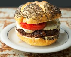 a hamburger with meat, cheese and tomatoes on a bun sitting on a white plate