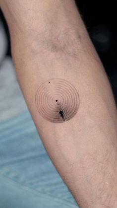 a man's arm with a small circle tattoo on the left side of his arm