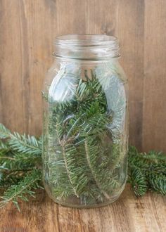 a mason jar filled with pine needles on top of a wooden table next to evergreen branches