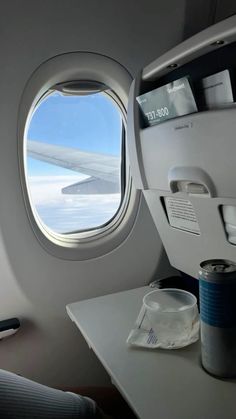 an airplane window looking out at the snow and ice below it, with a can of soda next to it