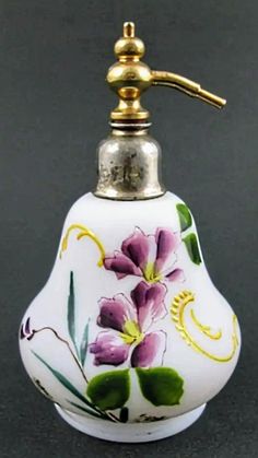 a white vase with purple flowers painted on it's side and a gold faucet