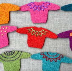 colorful sweaters made out of felt sitting on top of a cloth covered tablecloth