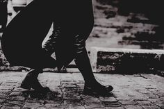 black and white photograph of person walking on cobblestone walkway with umbrella over head