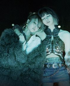 two young women laying next to each other in front of a black background, one with her arms around the other's head