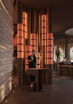 a woman sitting at a table in front of tall bamboo columns with lights on them