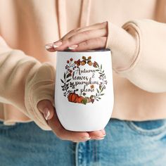 a woman holding a white coffee mug with autumn leaves and pumpkins on the inside