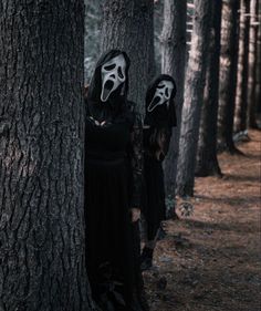 two women in black dresses and masks standing next to each other near some tall trees