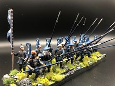 a group of toy soldiers with blue uniforms and spears on their heads, standing in front of a black background