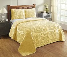 a bed with yellow bedspread and pillows on top of wooden floor next to window