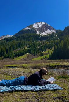 a person laying on a blanket reading a book in front of a snowy mountain range