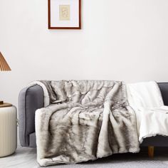 a grey couch with a white blanket on it and a brown lamp next to it