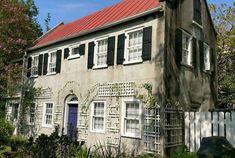 an old house with red roof and white shutters on the windows is surrounded by greenery