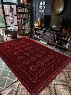 a living room with a large red rug on the floor and bookshelf in the background