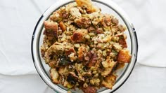 a glass bowl filled with stuffing on top of a white cloth covered table next to utensils