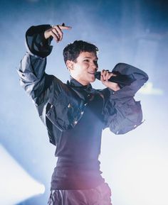 a male in a black jacket is holding his hand up to the side while singing